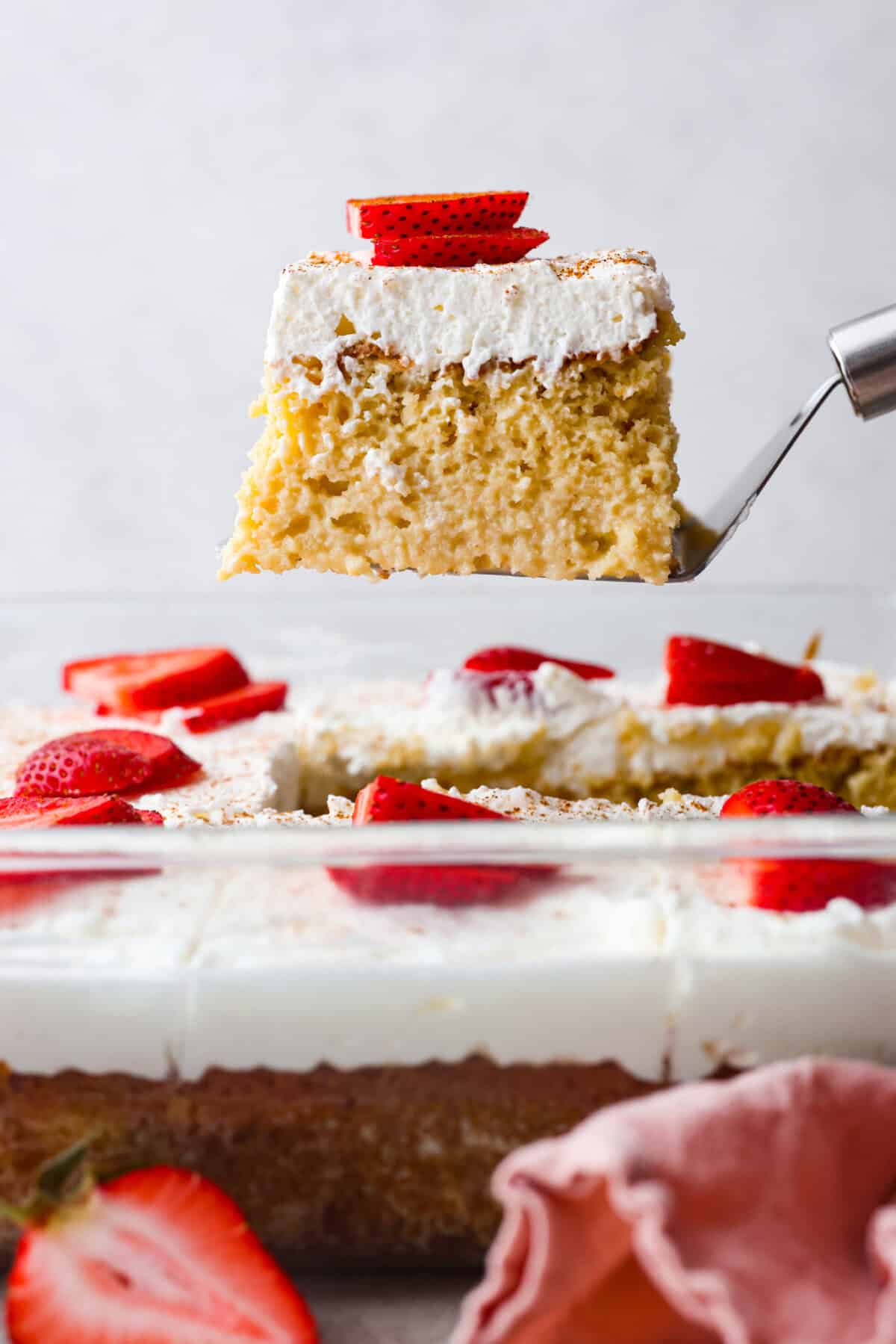 This tender Tres Leches cake is drenched in a three-milk mixture and is topped with fluffy whipped cream, cinnamon, or fresh fruit for a truly authentic Mexican dessert. Side shot of a slice of tres leches cake being lifted out of the pan.