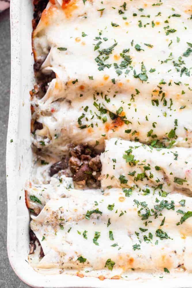 Salsa Verde Beef and Mushroom Enchiladas are SO easy to make, even on a weeknight! They're packed with a combo of beef and mushrooms, smothered in a creamy salsa verde sauce, and covered in shredded cheese. They'll become a new family favorite, guaranteed. Salsa Verde Beef and Mushroom Enchiladas in a pan.