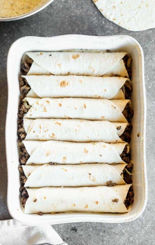 Salsa Verde Beef and Mushroom Enchiladas are SO easy to make, even on a weeknight! They're packed with a combo of beef and mushrooms, smothered in a creamy salsa verde sauce, and covered in shredded cheese. They'll become a new family favorite, guaranteed. Enchiladas in a baking dish.
