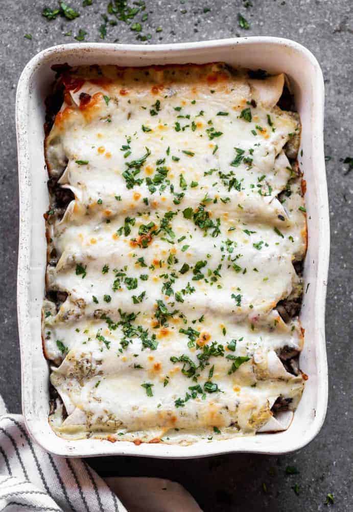 Salsa Verde Beef and Mushroom Enchiladas are SO easy to make, even on a weeknight! They're packed with a combo of beef and mushrooms, smothered in a creamy salsa verde sauce, and covered in shredded cheese. They'll become a new family favorite, guaranteed. Salsa Verde Beef and Mushroom Enchiladas in a baking pan.
