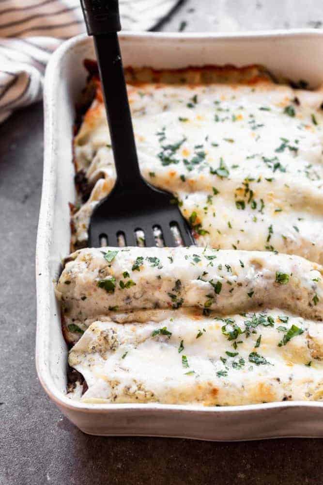 Salsa Verde Beef and Mushroom Enchiladas are SO easy to make, even on a weeknight! They're packed with a combo of beef and mushrooms, smothered in a creamy salsa verde sauce, and covered in shredded cheese. They'll become a new family favorite, guaranteed. A fork dipping into a pan of Salsa Verde Beef and Mushroom Enchiladas.