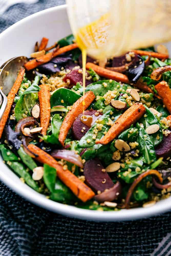 This roasted beet, quinoa, and carrot salad is packed with healthy and good-for-you ingredients! It's super flavorful and has the best lemon dressing! Pouring dressing on roasted beet, quinoa, and carrot salad.