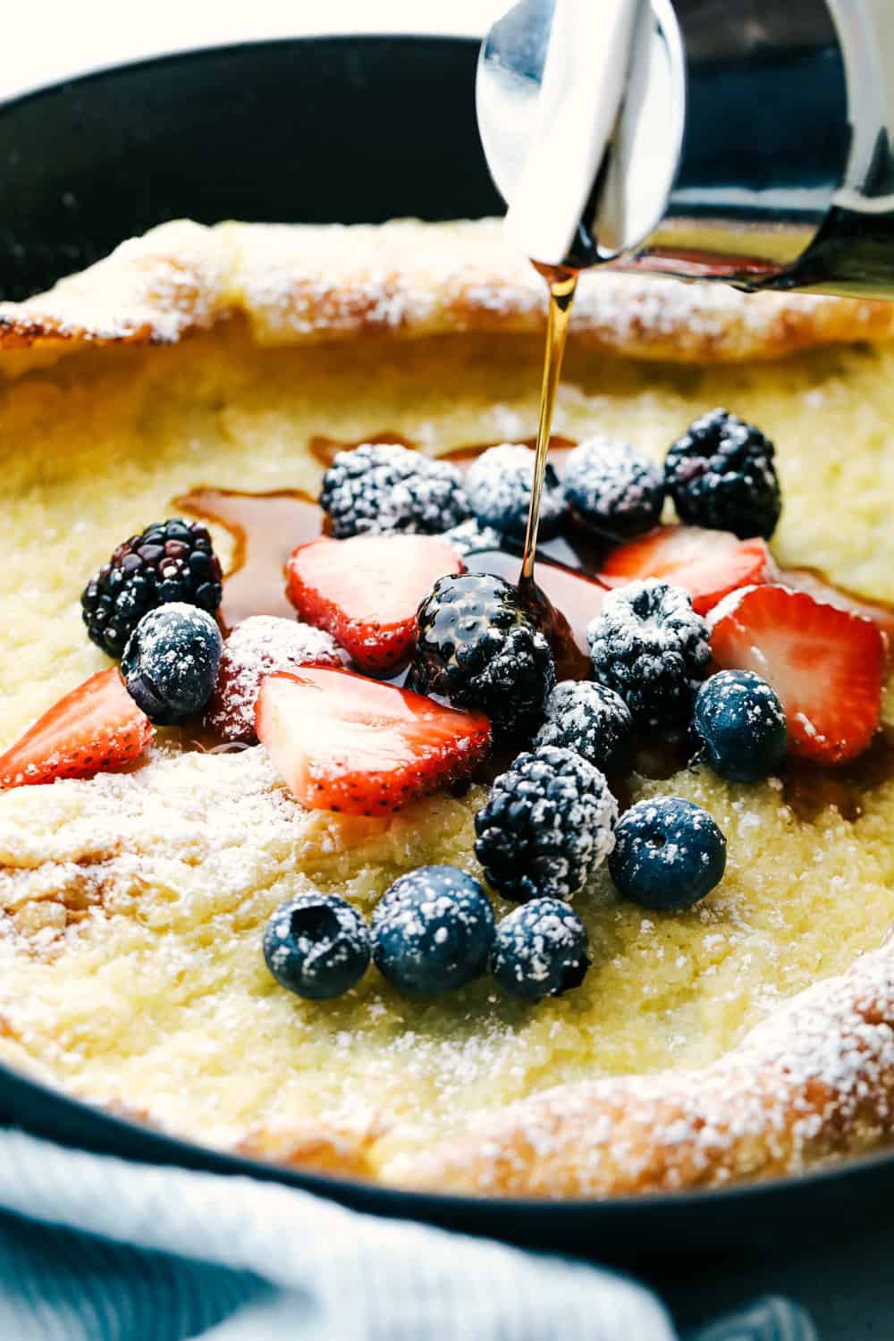 German Oven Pancake is a hot and puffy golden pancake that only requires 5 minutes of prep! This classic breakfast is always a huge hit at our house! German over pancake with fruit and syrup being poured overtop.