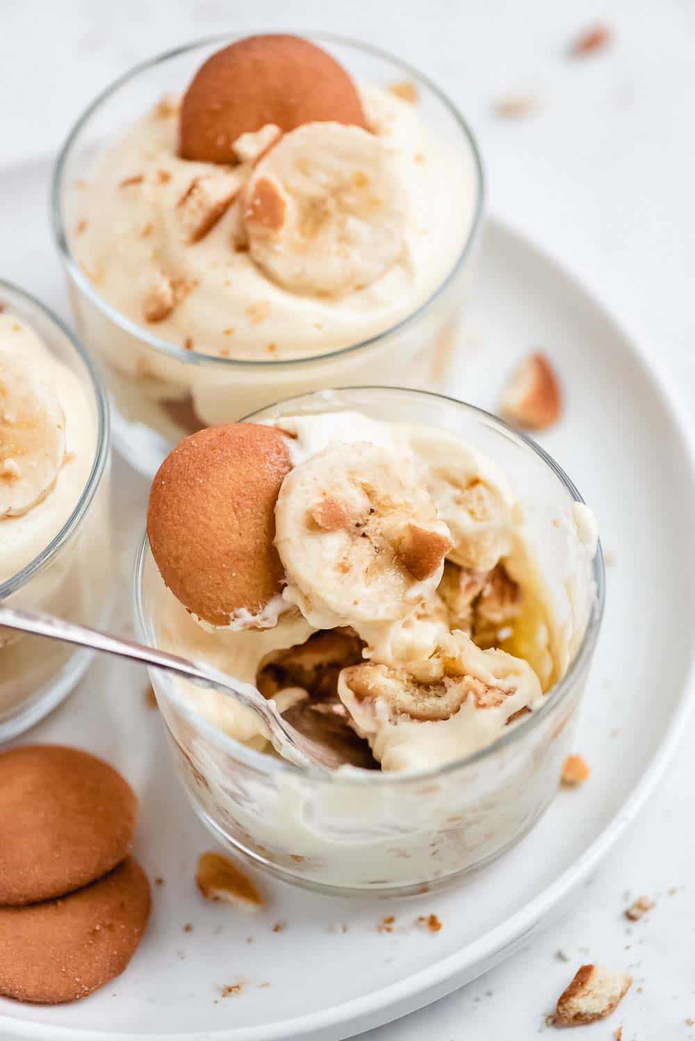 Magnolia Bakery Banana Pudding is a heavenly dessert made up of layers of creamy vanilla pudding, bananas, and Nilla Wafers. It's just like the famous New York City's Magnolia bakery recipe! There is a reason why it's so famous; it's seriously so good! Close-up shot of individual cup with a spoon in it and bites taken out of the cookies.