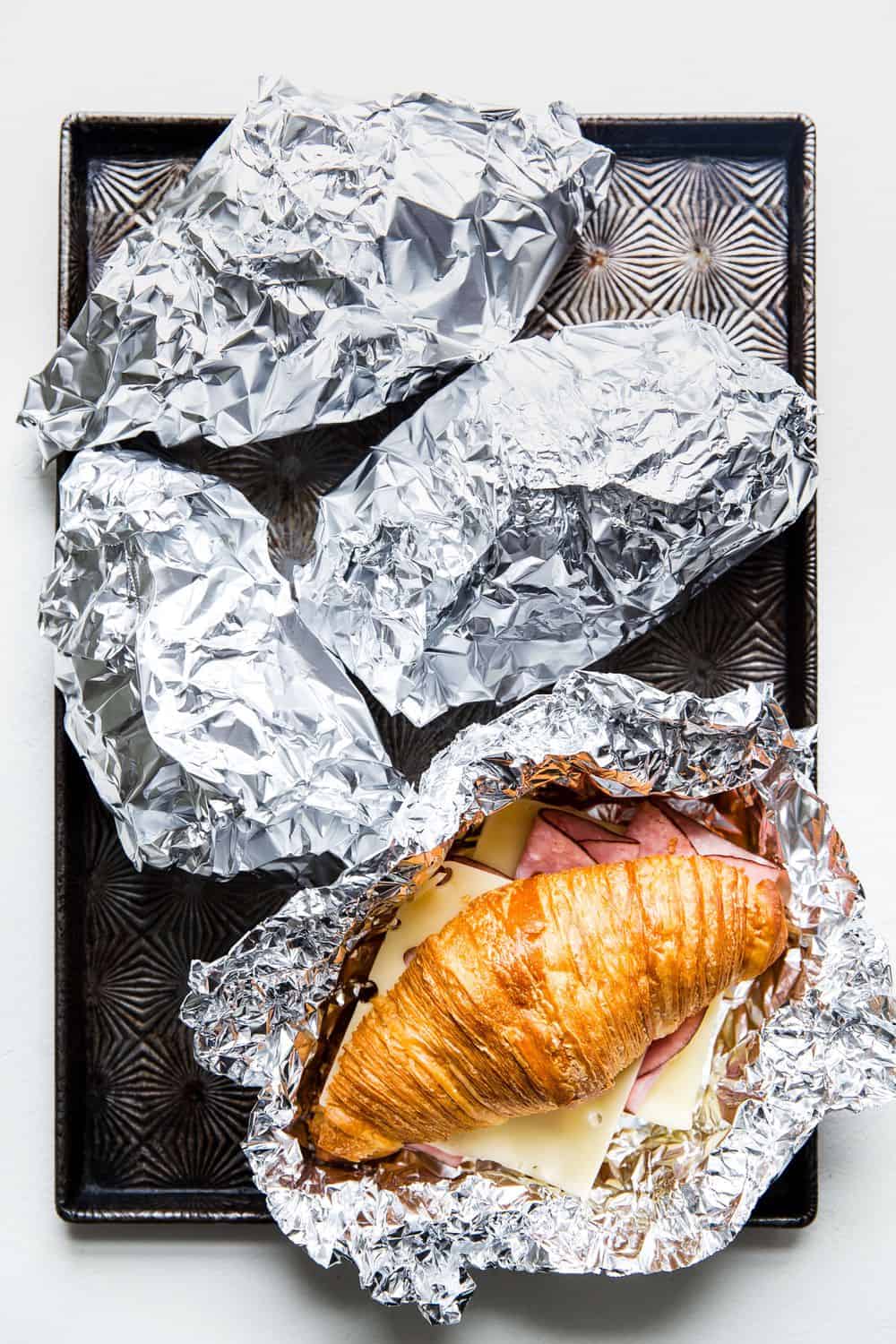 Monte Cristo Croissant Sandwich is a flaky croissant with melted Swiss cheese, decadent ham dipped in a raspberry jelly that will melt in your mouth with each bite! You will be in heaven with this sweet and savory sandwich! Wrapping a Monte Cristo Croissant Sandwich in tin foil.