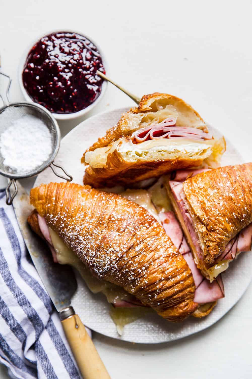 Monte Cristo Croissant Sandwich is a flaky croissant with melted Swiss cheese, decadent ham dipped in a raspberry jelly that will melt in your mouth with each bite! You will be in heaven with this sweet and savory sandwich! Monte Cristo Croissant Sandwiches on a plate.