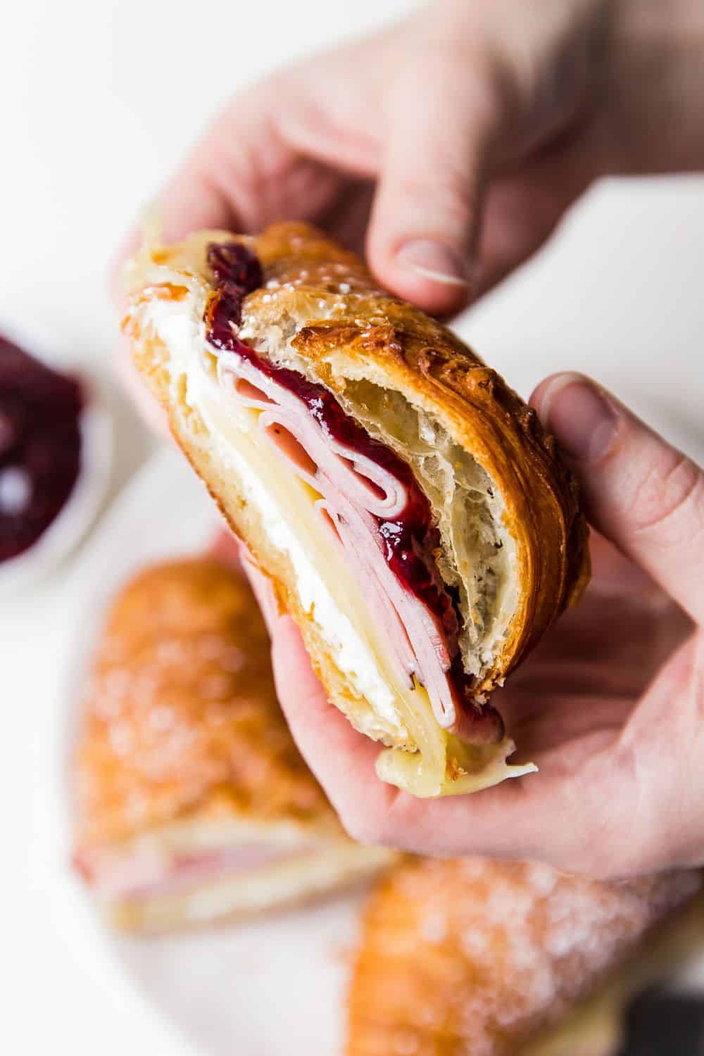 Monte Cristo Croissant Sandwich is a flaky croissant with melted Swiss cheese, decadent ham dipped in a raspberry jelly that will melt in your mouth with each bite! You will be in heaven with this sweet and savory sandwich! Side view of a monte cristo sandwich.