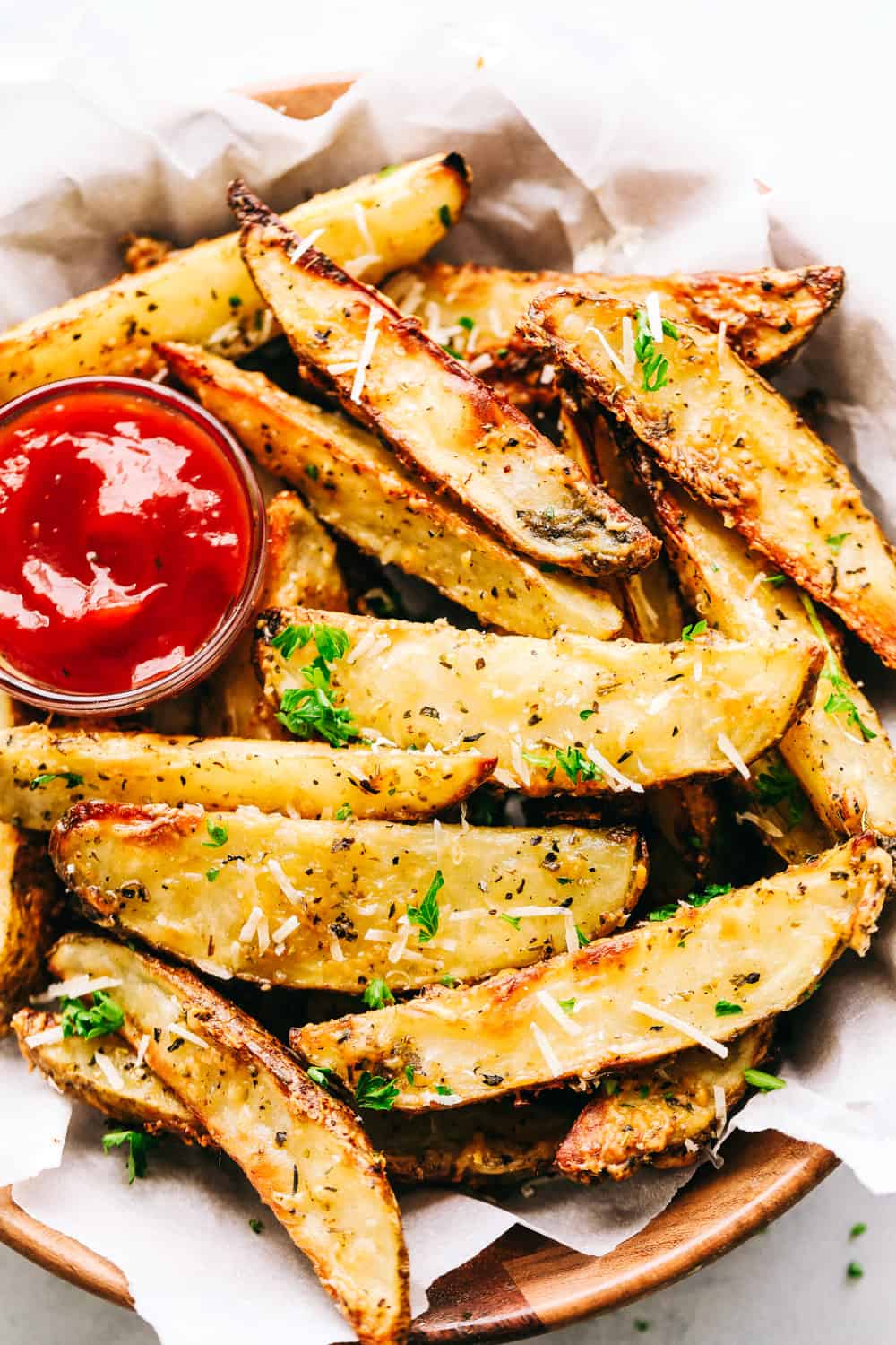 Baked parmesan garlic potato wedges are so incredibly easy and have the best savory flavor! These crispy wedges are roasted to perfection and guaranteed to be a huge hit. Grab your favorite dipping sauce and enjoy! Baked Parmesan Garlic Potato Wedges served with ketchup.