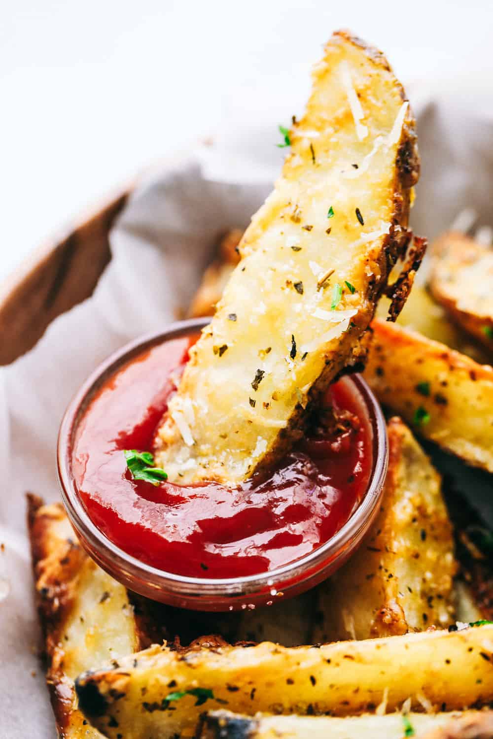 Baked parmesan garlic potato wedges are so incredibly easy and have the best savory flavor! These crispy wedges are roasted to perfection and guaranteed to be a huge hit. Grab your favorite dipping sauce and enjoy! Dipping a potato wedge in ketchup.