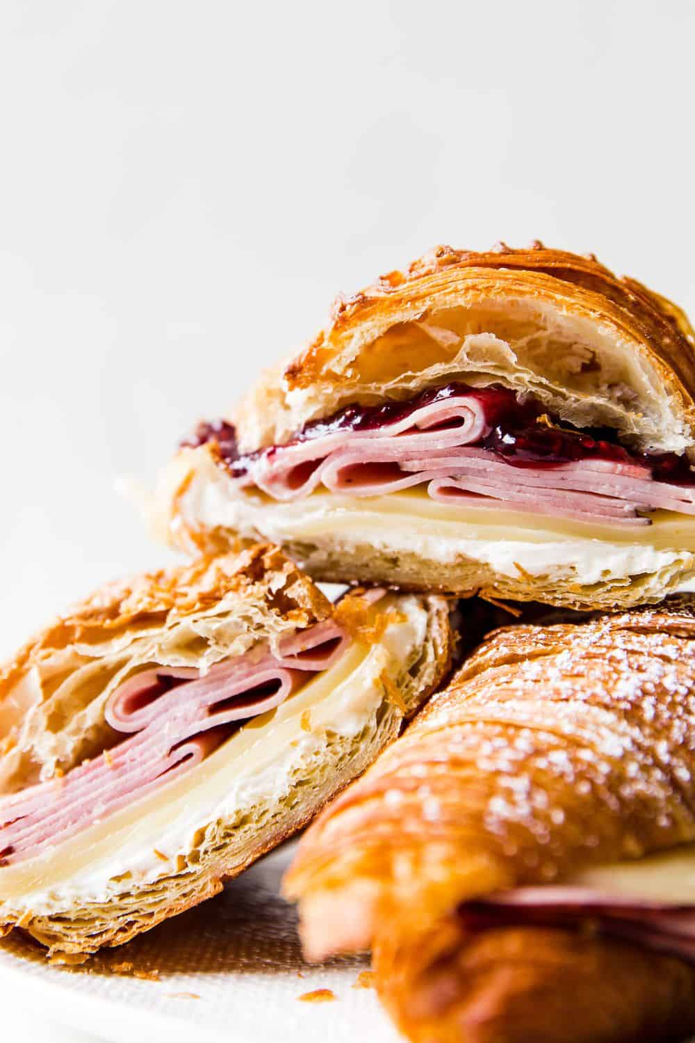 Monte Cristo Croissant Sandwich is a flaky croissant with melted Swiss cheese, decadent ham dipped in a raspberry jelly that will melt in your mouth with each bite! You will be in heaven with this sweet and savory sandwich! Monte Cristo Croissant Sandwiches stacked.