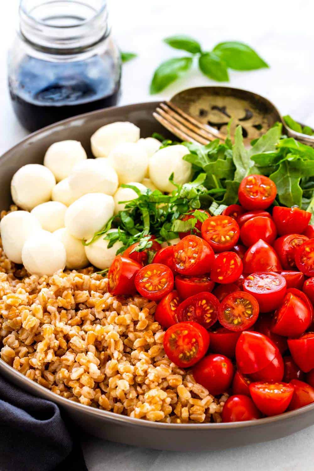 Farro Caprese Salad incorporates whole grains with an Italian classic pairing of juicy tomatoes and fresh buffalo mozzarella. Nutty farro is cooked until tender and then tossed with peppery arugula, cherry tomatoes, and soft ripened cheese. The salad is drizzled with a sweet and tangy balsamic reduction dressing. Farro Caprese Salad ingredients in a bowl