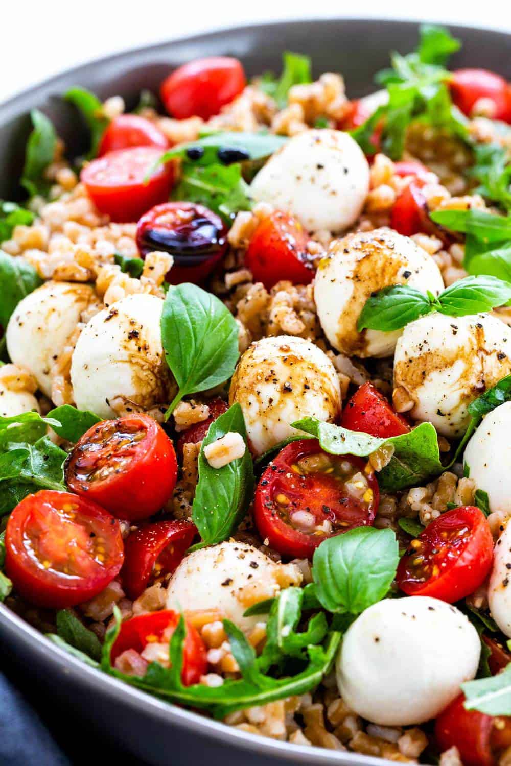 Farro Caprese Salad incorporates whole grains with an Italian classic pairing of juicy tomatoes and fresh buffalo mozzarella. Nutty farro is cooked until tender and then tossed with peppery arugula, cherry tomatoes, and soft ripened cheese. The salad is drizzled with a sweet and tangy balsamic reduction dressing. Farro Caprese Salad in a bowl.