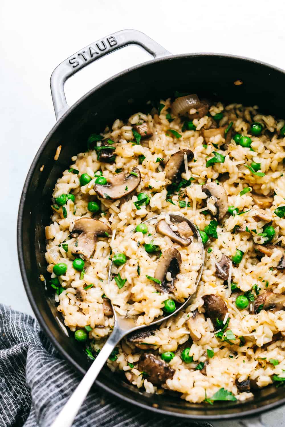 Mushroom Risottoย is soft short-grained rice that is cooked in broth with flavorful button mushrooms and sweet peas. The flavor combination is incredible and it's the perfect side dish for any protein! Mushroom risotto close up in a black pan with a spoon.