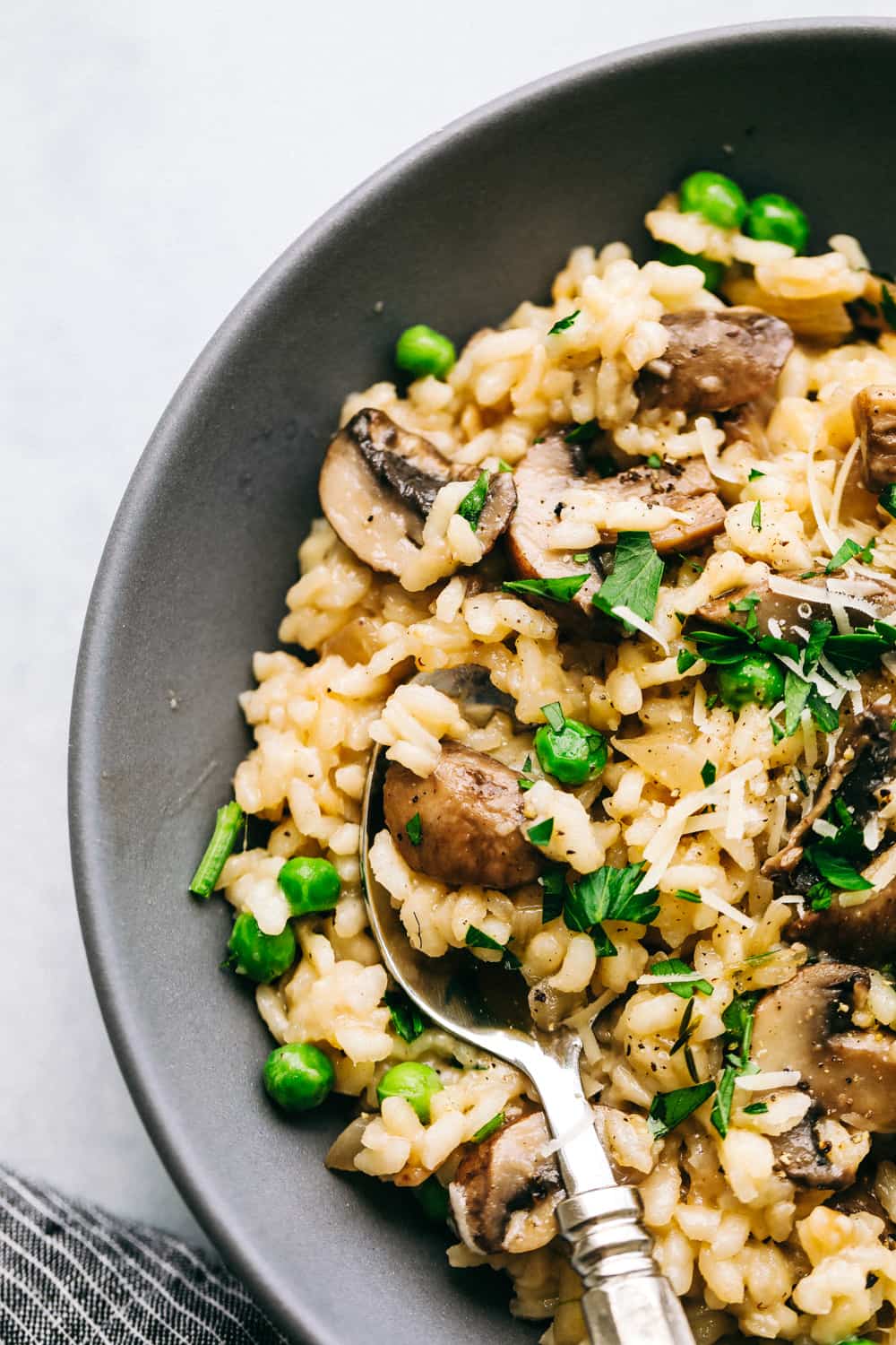 Mushroom Risottoย is soft short-grained rice that is cooked in broth with flavorful button mushrooms and sweet peas. The flavor combination is incredible and it's the perfect side dish for any protein! Creamy Mushroom Risotto in a black bowl with a spoon.