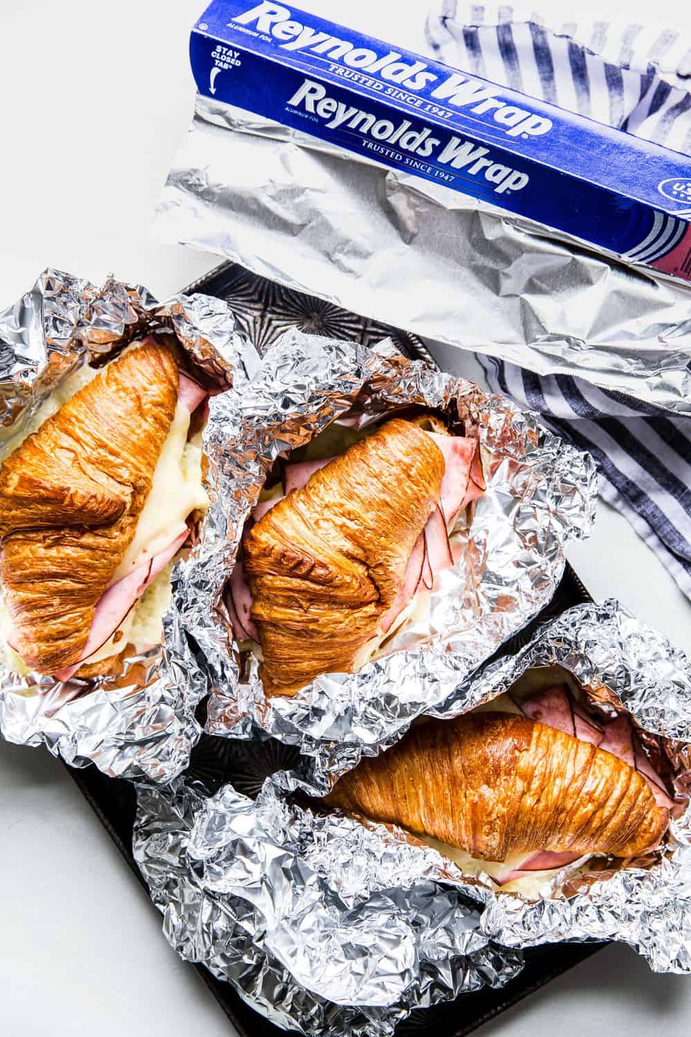 Monte Cristo Croissant Sandwich is a flaky croissant with melted Swiss cheese, decadent ham dipped in a raspberry jelly that will melt in your mouth with each bite! You will be in heaven with this sweet and savory sandwich! Monte Cristo Croissant Sandwich in tin foil wrappers.