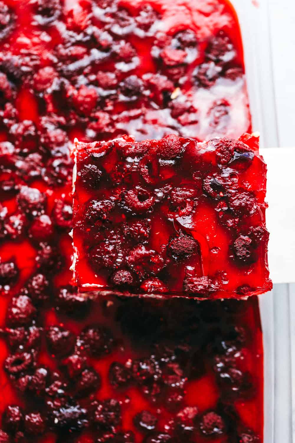 The Famous Raspberry Pretzel Salad is a classic sweet and savory dessert or side salad that everyone goes wild over. Plump raspberries, creamy whipped topping and a crunchy caramelized pretzel layered together making this a real treat! Cutting a slice of Raspberry Pretzel Salad