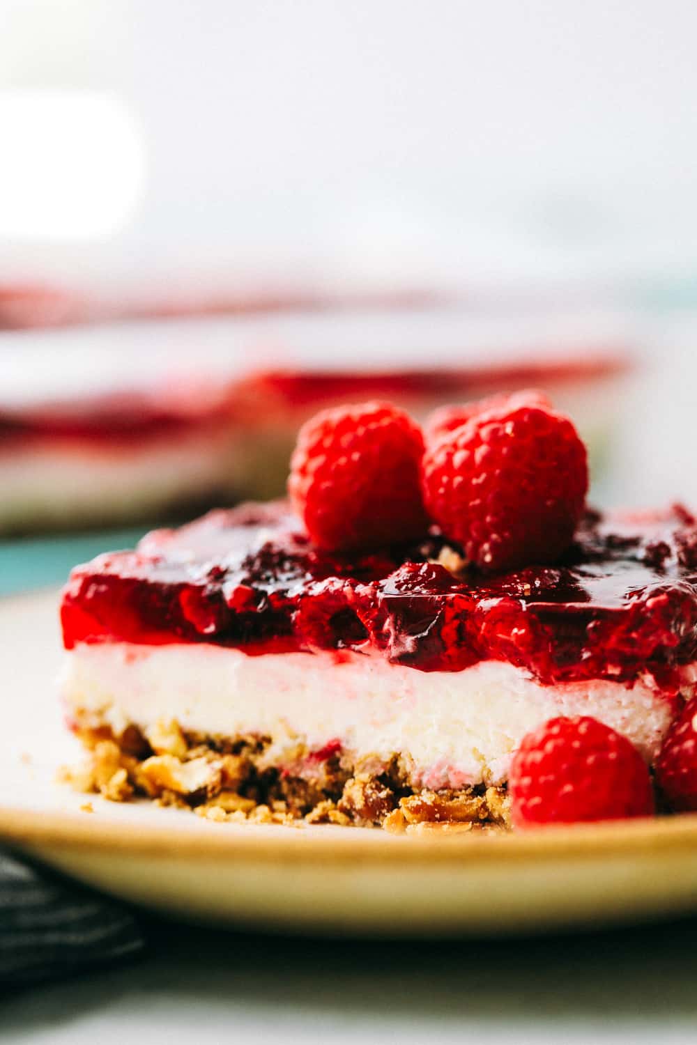 The Famous Raspberry Pretzel Salad is a classic sweet and savory dessert or side salad that everyone goes wild over. Plump raspberries, creamy whipped topping and a crunchy caramelized pretzel layered together making this a real treat! A slice of raspberry pretzel salad on a plate.