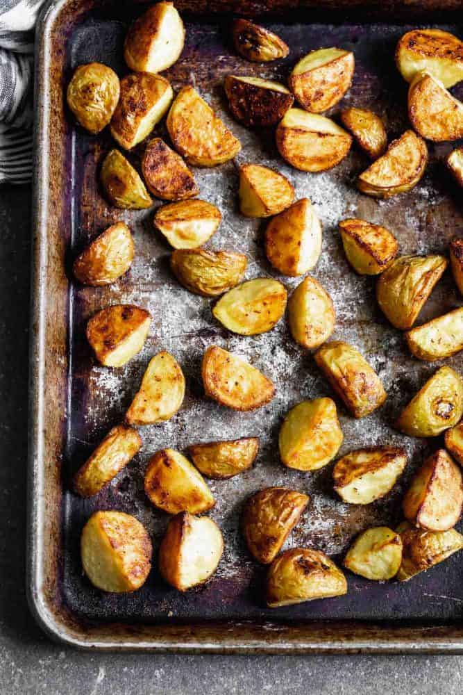 These Crispy Potatoes with Pesto and Parmesan are SO easy to make and go with everything! Store-bought pesto is tossed with easy oven-roasted potatoes, and then sprinkled with parmesan cheese. A crowd favorite! Potatoes after cooking on a sheet pan before seasoning.