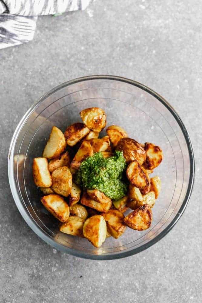 These Crispy Potatoes with Pesto and Parmesan are SO easy to make and go with everything! Store-bought pesto is tossed with easy oven-roasted potatoes, and then sprinkled with parmesan cheese. A crowd favorite! Adding seasoning to potatoes.