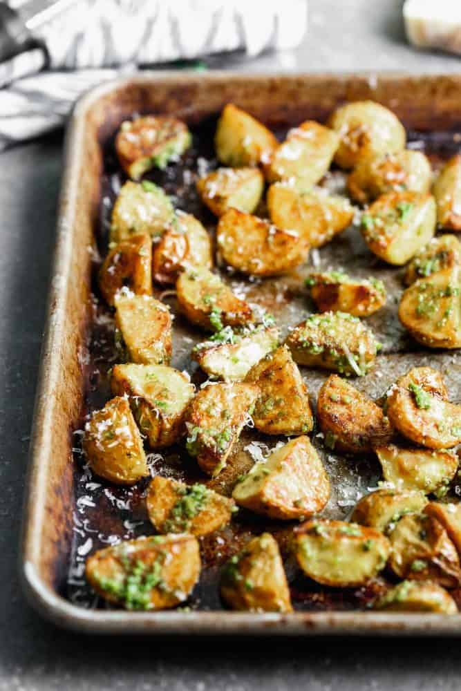 These Crispy Potatoes with Pesto and Parmesan are SO easy to make and go with everything! Store-bought pesto is tossed with easy oven-roasted potatoes, and then sprinkled with parmesan cheese. A crowd favorite! Finished potatoes on a sheet pan.