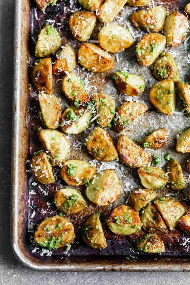 These Crispy Potatoes with Pesto and Parmesan are SO easy to make and go with everything! Store-bought pesto is tossed with easy oven-roasted potatoes, and then sprinkled with parmesan cheese. A crowd favorite! Finished potatoes on a sheet pan.