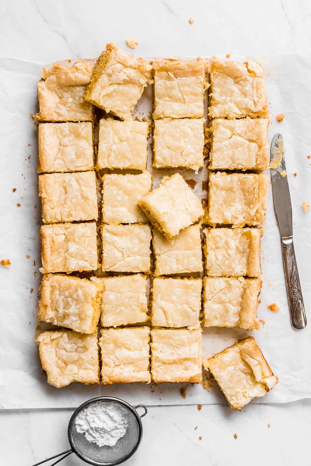 Neiman Marcus Bars are the easiest indulgent treat! These addicting bars are a mix between a blondie bar and cheesecake square but gooey and have a shiny crispy top like a brownie. This is the perfect dessert for sharing with family and friends! Neiman Marcus Bars cut into squares.