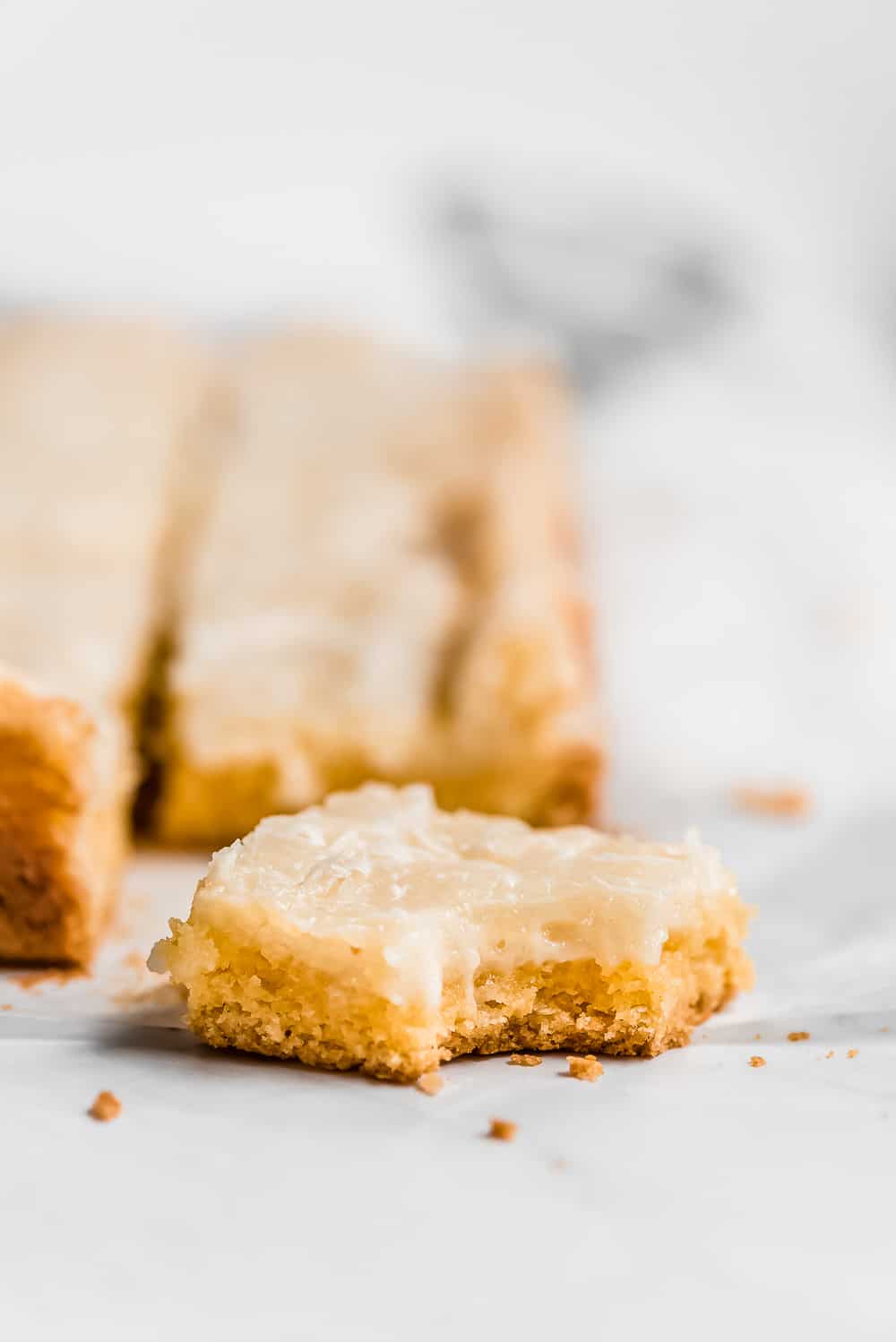 Neiman Marcus Bars are the easiest indulgent treat! These addicting bars are a mix between a blondie bar and cheesecake square but gooey and have a shiny crispy top like a brownie. This is the perfect dessert for sharing with family and friends! Close up on a neiman marcus bar with one bite taken out.
