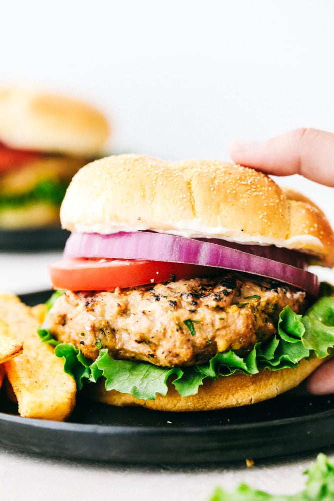 These Turkey Burgers are loaded with flavor and perfect for summer grilling! Easy to prep ahead and freeze to enjoy all summer long. #recipe #burger #grilling Turkey burger in a bun with red onion, tomatoes and fries on the side.