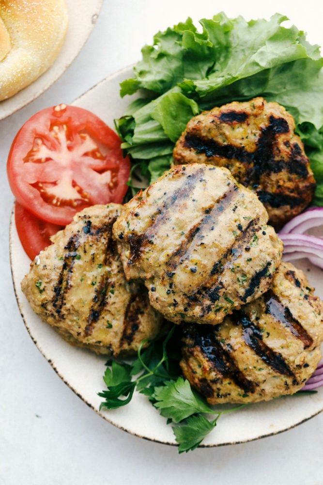 These Turkey Burgers are loaded with flavor and perfect for summer grilling! Easy to prep ahead and freeze to enjoy all summer long. #recipe #burger #grilling Grilled turkey burgers on a plate with lettuce, tomatoes and onions.