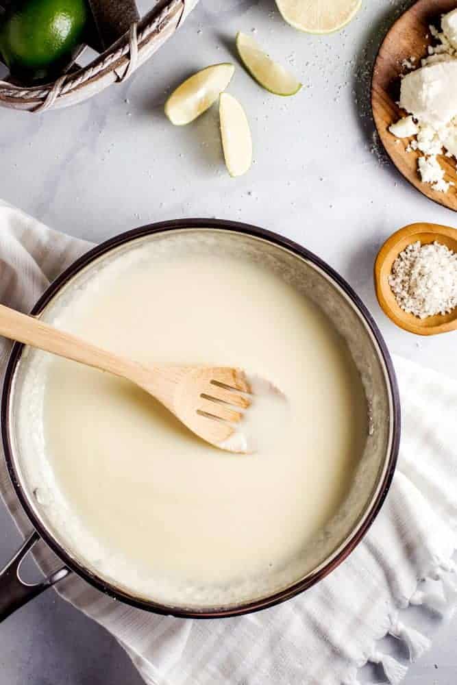 This Queso Chicken Skillet has the potential to become your families new favorite weeknight dinner. Creamy queso melted together with tender chicken, diced chilis and tomatoes, all mixed into tasty yellow rice create the perfect cheesy dinner. Making queso in a pot and stirring with a wooden spoon.