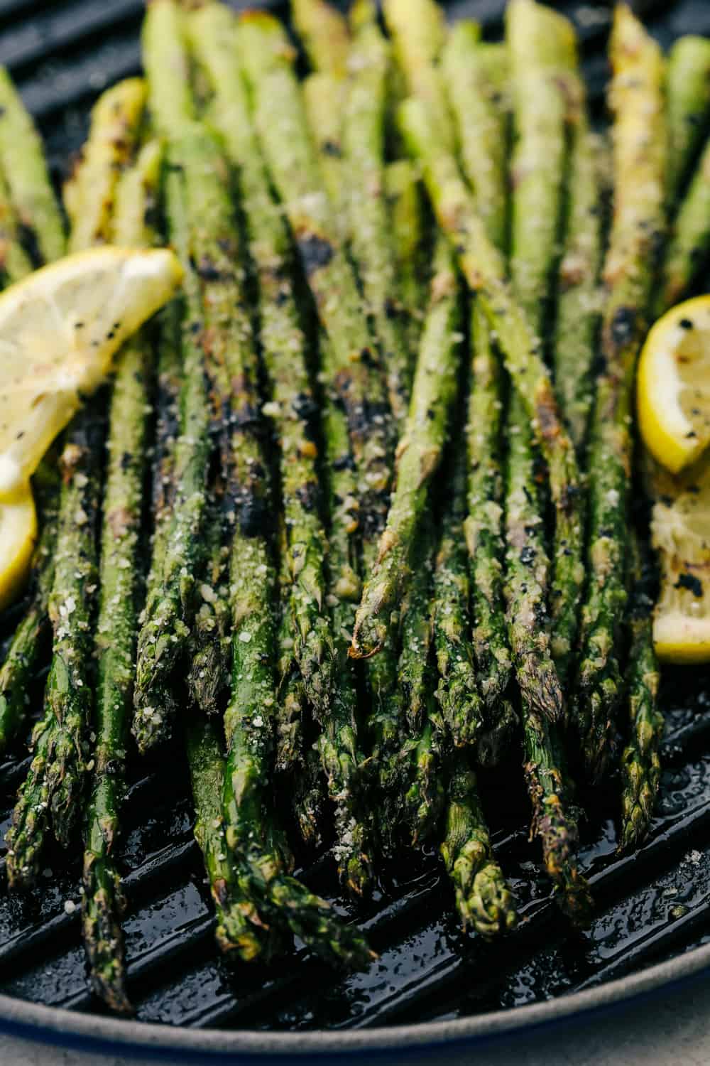 Fresh Asparagusย that is grilled gives you char marks and a smoky flavor that is amazing! Within minutes you have tender asparagus coated in parmesan and garlic that will become a family favorite! Asparagus on the grill plate with lemon wedges on the side.