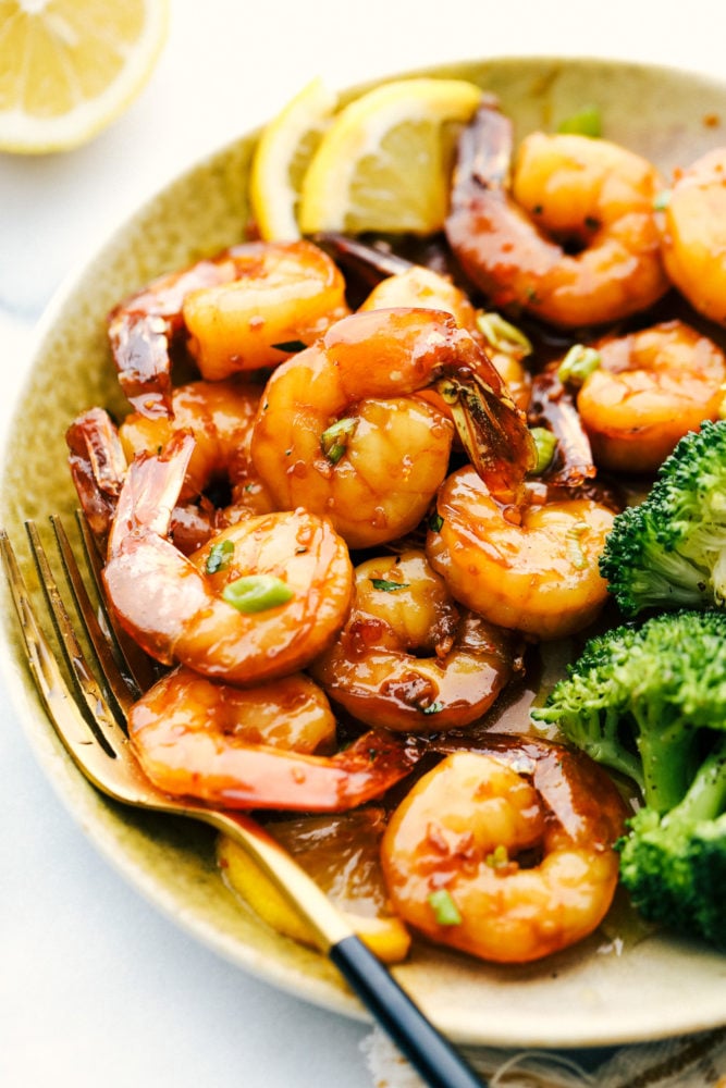 Sticky Honey Garlic Butter Shrimp are coated in the most amazing sticky honey garlic butter soy sauce. This is a quick 20 minute meal that you will make again and again! Sticky honey garlic butter shrimp on a plate with broccoli and lemon garnishes.