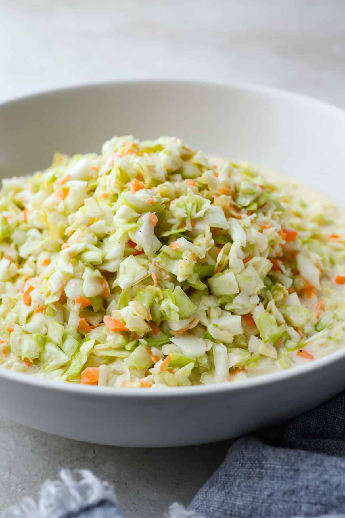 My Copycat KFC Coleslaw is so spot-on, youโll think itโs the real deal! Crunchy, creamy, tangy, and perfect for any BBQ, everyone will want the recipe! Angle shot of copycat KFC coleslaw in a serving dish.