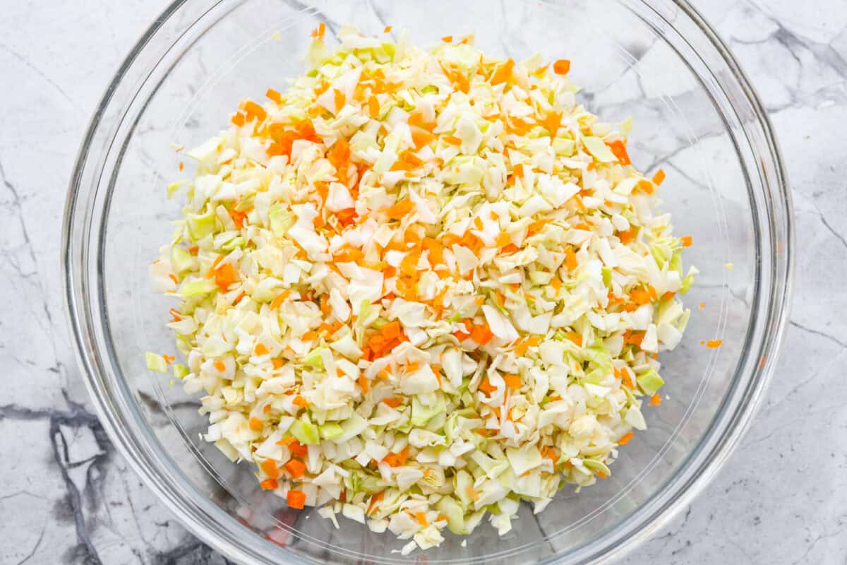 My Copycat KFC Coleslaw is so spot-on, youโll think itโs the real deal! Crunchy, creamy, tangy, and perfect for any BBQ, everyone will want the recipe! Overhead shot of chopped carrots and cabbage in a mixing bowl.