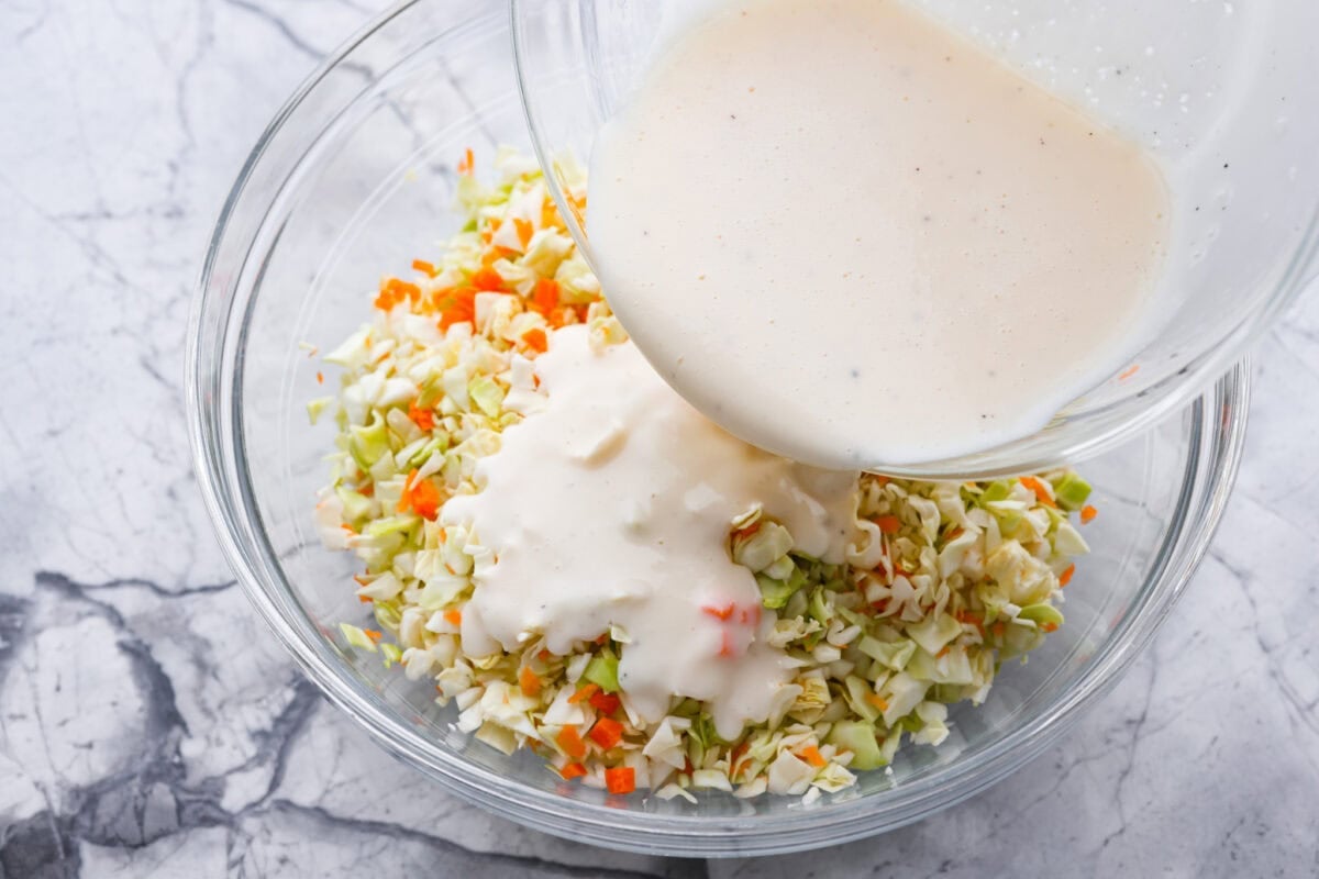 My Copycat KFC Coleslaw is so spot-on, youโll think itโs the real deal! Crunchy, creamy, tangy, and perfect for any BBQ, everyone will want the recipe! Dressing being poured over the cabbage mixture.