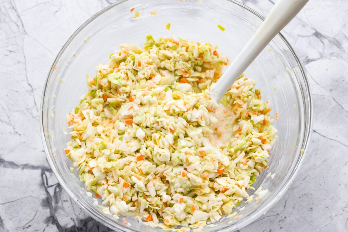 My Copycat KFC Coleslaw is so spot-on, youโll think itโs the real deal! Crunchy, creamy, tangy, and perfect for any BBQ, everyone will want the recipe! Cabbage mixture and dressing being stirred together.