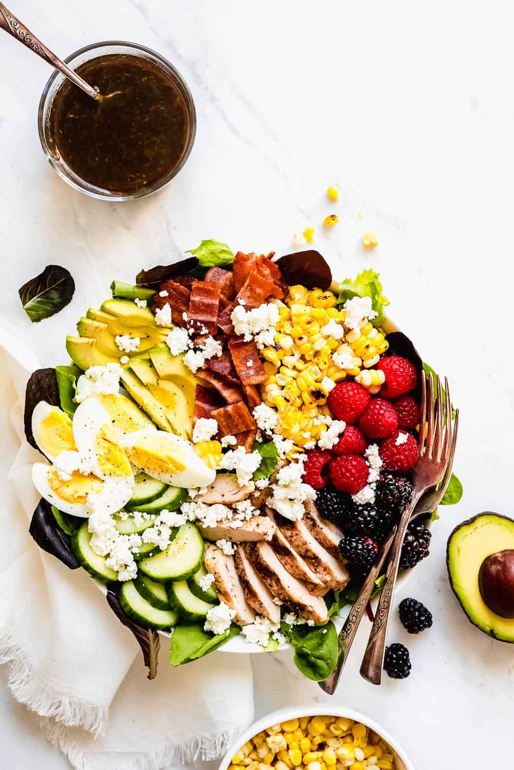 Summer Cobb Salad is filled with fresh summer fruits and veggies. It's loaded with grilled chicken, bacon, hard boiled eggs, avocado, goat cheese, berries, cucumber, grilled corn and tossed in a simple balsamic lime vinegar dressing. Every bite is refreshing, bright, and summery! Summer cobb salad in a bowl.