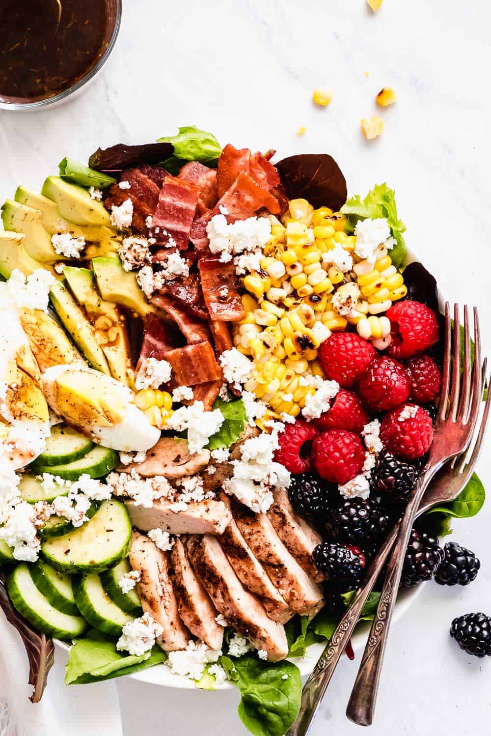 Summer Cobb Salad is filled with fresh summer fruits and veggies. It's loaded with grilled chicken, bacon, hard boiled eggs, avocado, goat cheese, berries, cucumber, grilled corn and tossed in a simple balsamic lime vinegar dressing. Every bite is refreshing, bright, and summery! Summer Cobb Salad on a plate.
