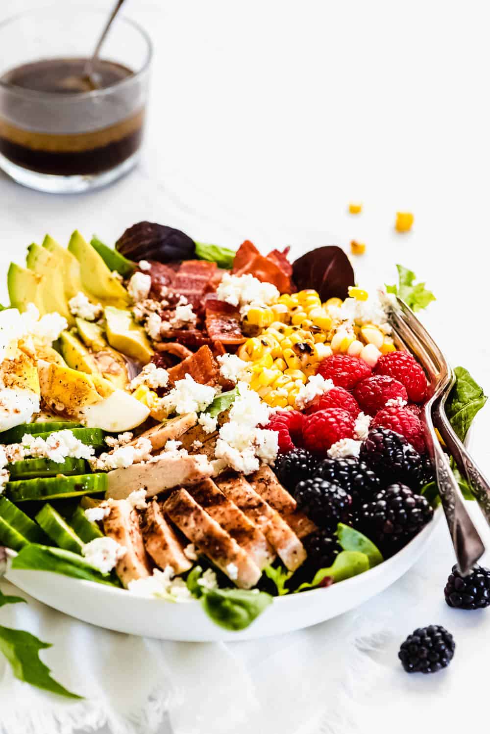 Summer Cobb Salad is filled with fresh summer fruits and veggies. It's loaded with grilled chicken, bacon, hard boiled eggs, avocado, goat cheese, berries, cucumber, grilled corn and tossed in a simple balsamic lime vinegar dressing. Every bite is refreshing, bright, and summery! Summer cobb salad in a bowl.