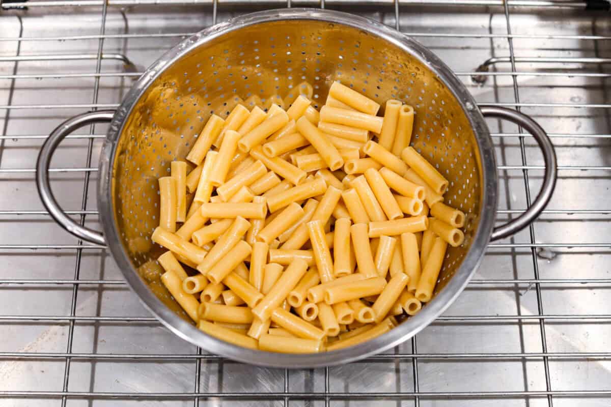 This cheesy baked ziti is baked to perfection with al dente noodles, spicy pepperoni, flavorful sausage, and smothered in melty cheese. It comes together quickly and easily and can be made ahead of time for busy weeknights! Overhead shot of cooked pasta in a colander.