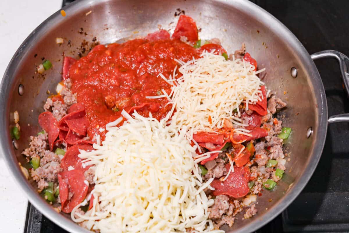 This cheesy baked ziti is baked to perfection with al dente noodles, spicy pepperoni, flavorful sausage, and smothered in melty cheese. It comes together quickly and easily and can be made ahead of time for busy weeknights! Overhead shot of meat and veggie mixture with sauce and cheeses.