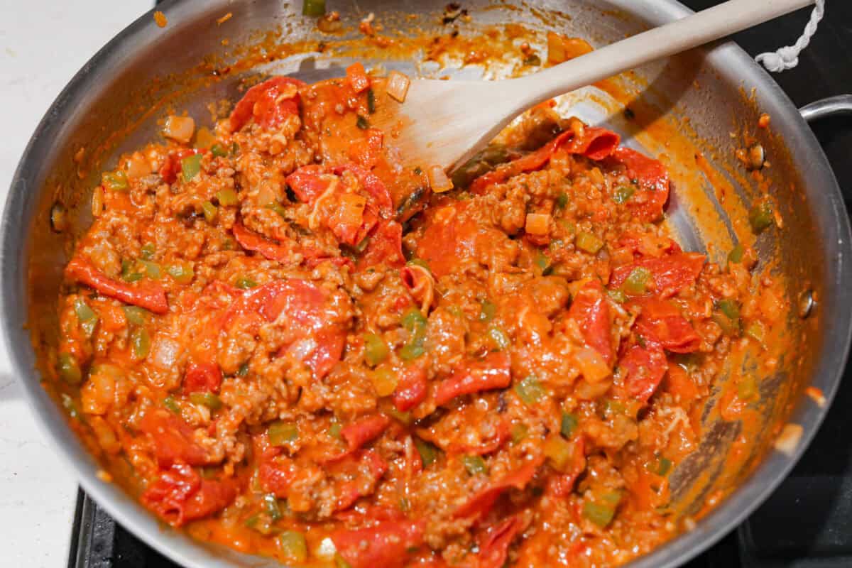 This cheesy baked ziti is baked to perfection with al dente noodles, spicy pepperoni, flavorful sausage, and smothered in melty cheese. It comes together quickly and easily and can be made ahead of time for busy weeknights! Overhead shot of meat and veggie mixture mixed in with cheeses and sauce.