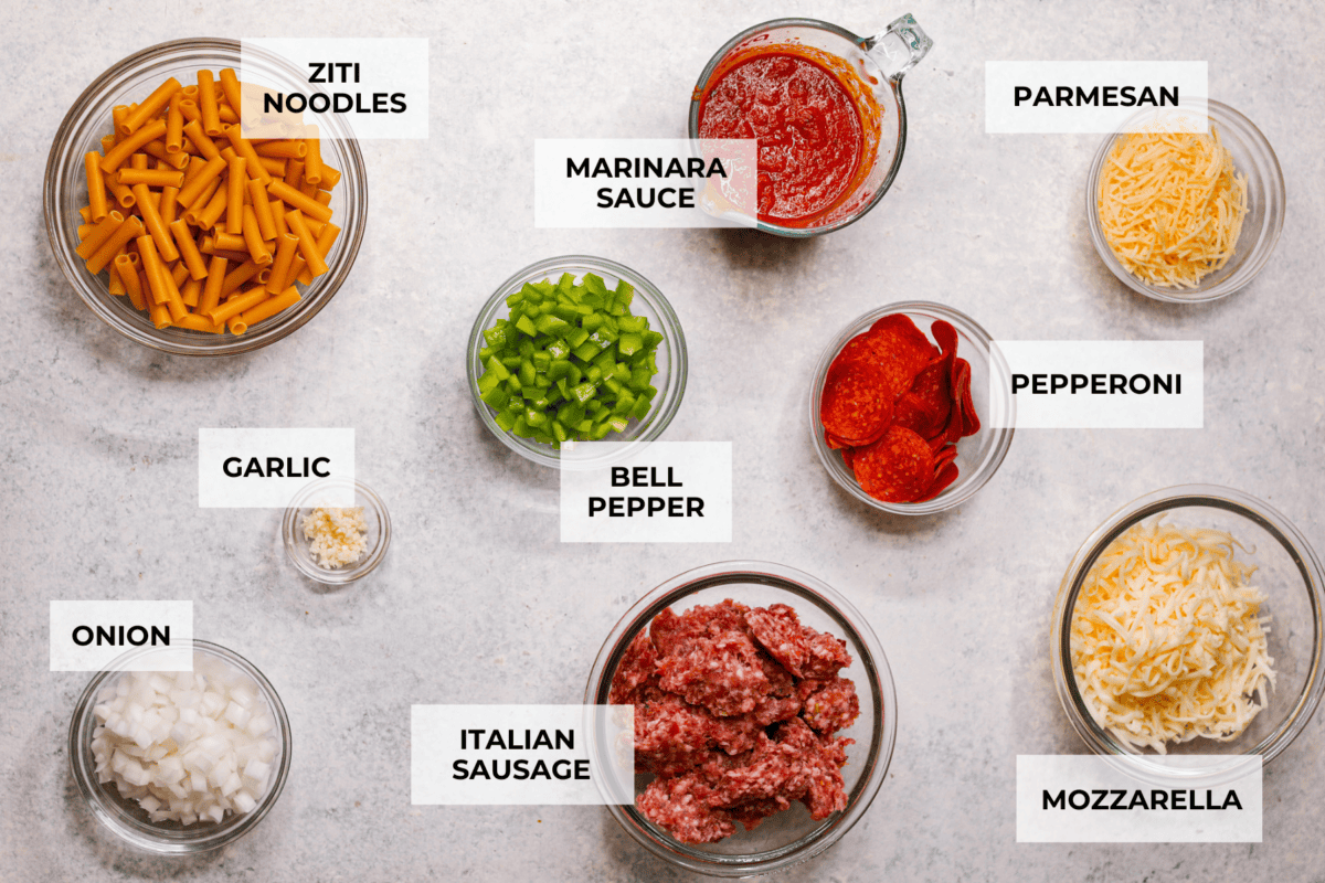 This cheesy baked ziti is baked to perfection with al dente noodles, spicy pepperoni, flavorful sausage, and smothered in melty cheese. It comes together quickly and easily and can be made ahead of time for busy weeknights! Overhead shot of labeled ingredients.