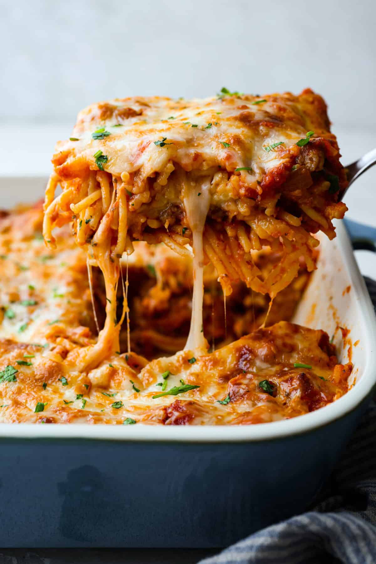 Baked spaghetti is the ultimate comfort food, with noodles that soak up all of the rich sauce as they finish cooking, making every bite extra flavorful. Plus, itโs a lifesaver on busy days. You can prep it ahead, pop it in the oven, and still have a cozy, home-cooked meal without the stress! Side shot of someone lifting a piece of baked spaghetti out of the pan.