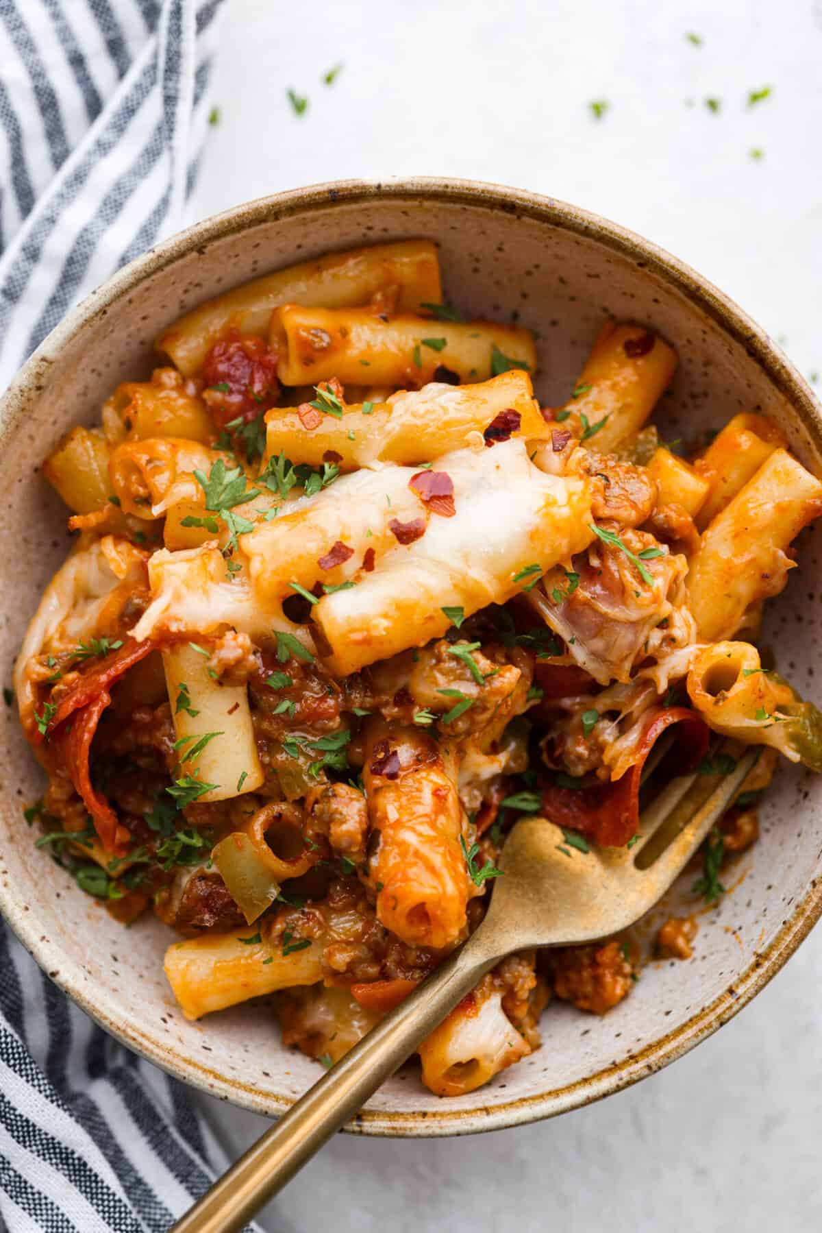 This cheesy baked ziti is baked to perfection with al dente noodles, spicy pepperoni, flavorful sausage, and smothered in melty cheese. It comes together quickly and easily and can be made ahead of time for busy weeknights! Overhead shot of plated cheesy baked ziti.