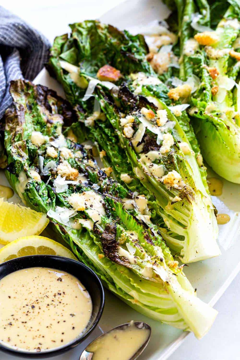 Grilled Caesar Salad with leafy sections of romaine seared on the barbecue to create a lightly charred texture then drizzled in homemade dressing. Grilled Caesar Salad with croutons on top