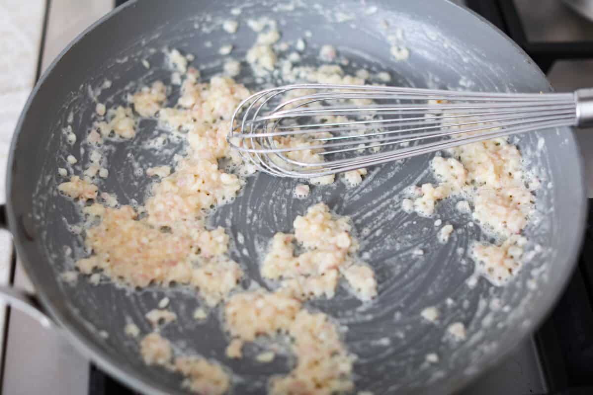 Creamed Spinach is a classic and delicious side dish! It is loaded with fresh spinach and has the creamiest garlic parmesan sauce. Serve it alongside any meal! Third photo of the shallots and garlic cooking in a pan.