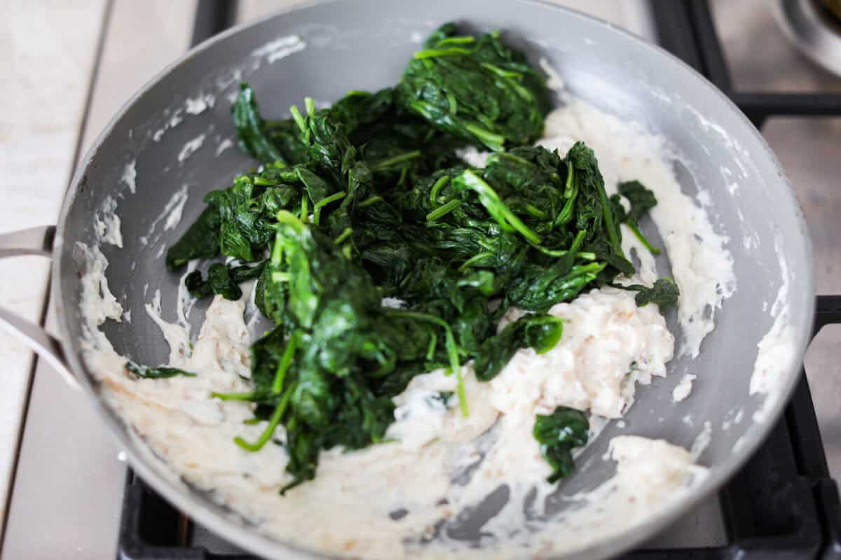 Creamed Spinach is a classic and delicious side dish! It is loaded with fresh spinach and has the creamiest garlic parmesan sauce. Serve it alongside any meal! Sixth photo of the cooked spinach stirring into the creamy mixture.