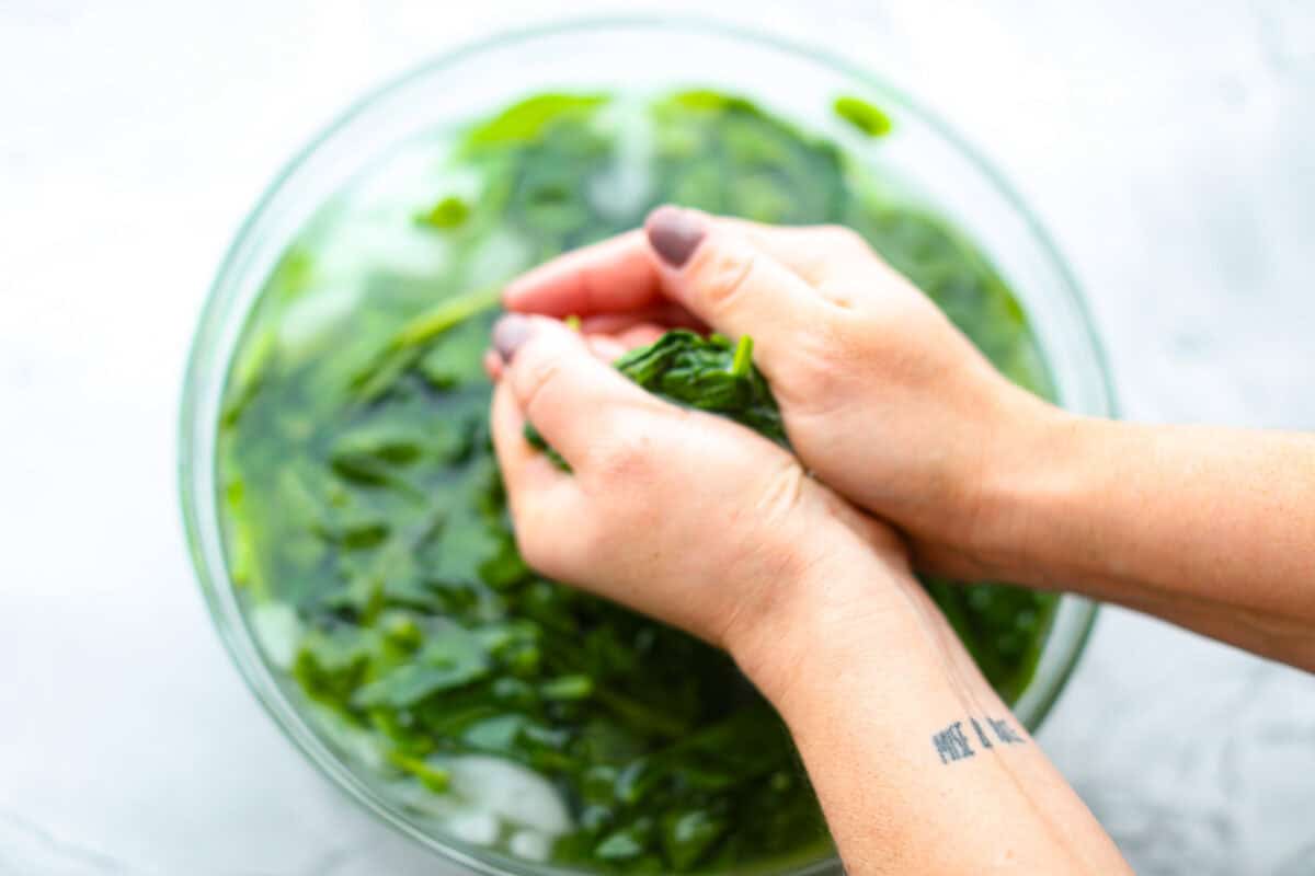 Creamed Spinach is a classic and delicious side dish! It is loaded with fresh spinach and has the creamiest garlic parmesan sauce. Serve it alongside any meal! Second photo of squeezing and draining the spinach.