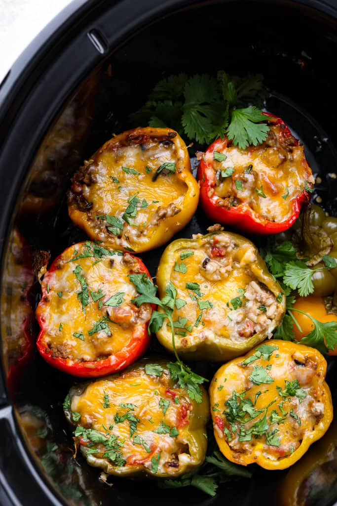 Slow cooker stuffed bell peppers are packed with ground beef, wild rice, diced tomatoes, soft black beans, and melty cheese. They cook to perfection in the slow cooker and make a healthy, delicious dinner your whole family will love! Overhead shot of slow cooker stuffed bell peppers.